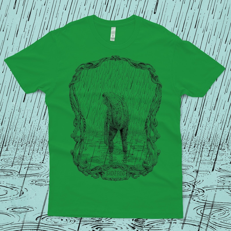 An original drawing of a sad frog standing in the rain, surrounded by an ornate border. Screen printed onto a Kelly green, Next Level brand T-shirt.