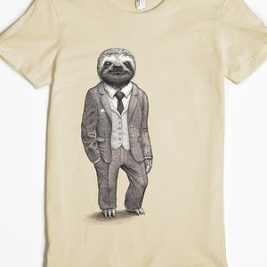 Puede incluir: Una camiseta beige con un gr&aacute;fico de un perezoso con traje y corbata. El perezoso est&aacute; de pie con las manos en los bolsillos.
