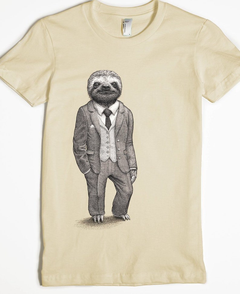 Puede incluir: Una camiseta beige con un gr&aacute;fico de un perezoso con traje y corbata. El perezoso est&aacute; de pie con las manos en los bolsillos.