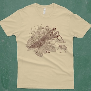 An intricate drawing of a praying mantis, snail, beetle and mushrooms, screen printed on a cream colored men's T-shirt in front of a turquoise backdrop