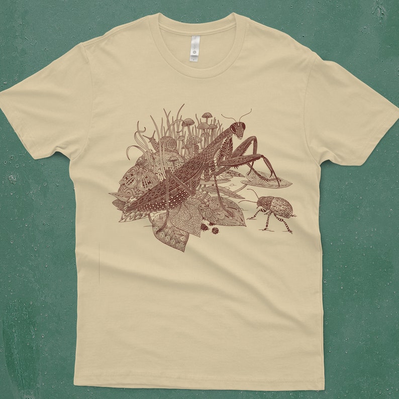 An intricate drawing of a praying mantis, snail, beetle and mushrooms, screen printed on a cream colored men's T-shirt in front of a turquoise backdrop