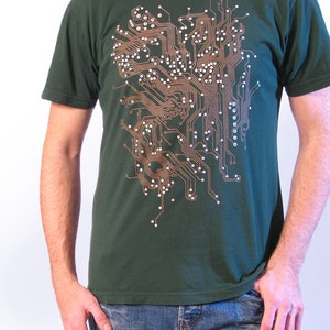 May include: Dark green t-shirt with a copper-coloured circuit board design and white dots. The graphic covers the front. The shirt is paired with blue jeans.