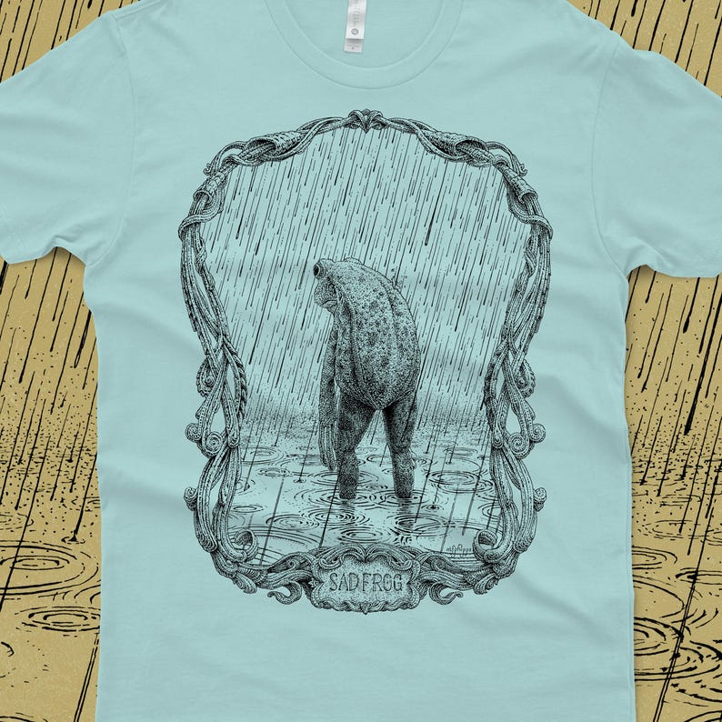 A drawing of a sad frog standing in the rain. Screen printed onto a blue, Next Level brand T-shirt.