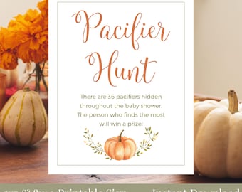May include: A white sign with the words "Pacifier Hunt" in orange script. The sign includes text about a baby shower game and a pumpkin illustration. The sign is labeled "5x7 & 8x10 Printable Sign".