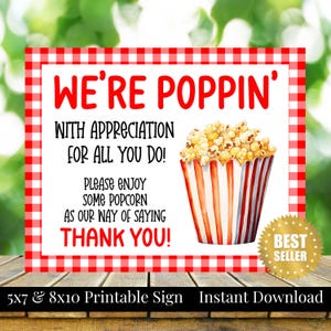 Op de afbeelding: Een printbaar bord met een rood-witte geruite rand. Het bord luidt "WE'RE POPPIN'" en bevat de tekst "WITH APPRECIATION FOR ALL YOU DO! PLEASE ENJOY SOME POPCORN AS OUR WAY OF SAYING THANK YOU!" Een aquarel illustratie van popcorn in een gestreepte bak is ook aanwezig.