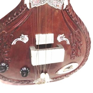 May include: A close-up of a brown sitar, a traditional Indian stringed instrument. The instrument features intricate carvings, decorative accents, and tuning knobs. The strings are visible, along with the sound hole.