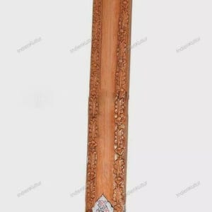 Könnte beinhalten: Gezeigt wird ein Flat Tanpuri, ein traditionelles indisches Saiteninstrument. Das Holzinstrument weist auf Hals und Korpus aufwendige Schnitzereien mit dekorativen Elementen und Wirbeln auf. Das Instrument hat eine hellbraune Farbe.