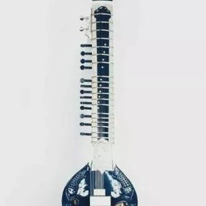 May include: A sitar, a long-necked plucked stringed instrument, is displayed against a white background. The instrument features a dark blue body with ornate carvings and a long neck with frets. The headstock and tuning pegs are visible.