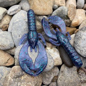 May include: Two purple and teal crawfish-shaped fishing lures with glitter.