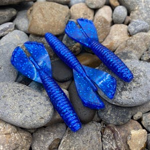 Peut inclure: Trois leurres de pêche en plastique souple bleu avec une finition pailletée. Les leurres ont une queue fendue.
