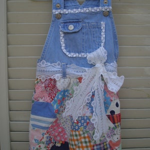 May include: A blue denim overall dress with a white lace trim and a patchwork skirt. The skirt is made of various colorful fabrics, including red, pink, blue, and green.