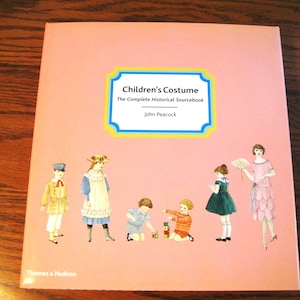 May include: A pink book titled "Children's Costume: The Complete Historical Sourcebook" by John Peacock. The cover features illustrations of children in various historical costumes.