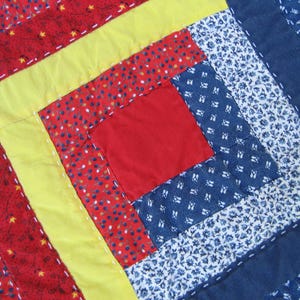 May include: A quilt made of red, yellow, blue, and white fabric with a geometric pattern. The quilt is made of squares and rectangles, and the fabric is patterned with small white dots on a blue background, small red dots on a white background, and small yellow dots on a red background.