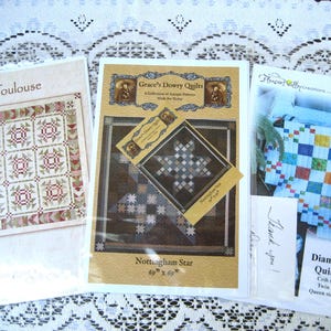 May include: Three quilt pattern packets. The "Toulouse" pattern features a red and beige design. The "Nottingham Star" pattern is 69" x 69". The "Diamond Patch" pattern is available in crib, twin, and queen sizes.