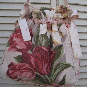 May include: A pink and green floral tote bag with a drawstring closure and lace trim. The bag has a long strap and is made of a soft, textured fabric.