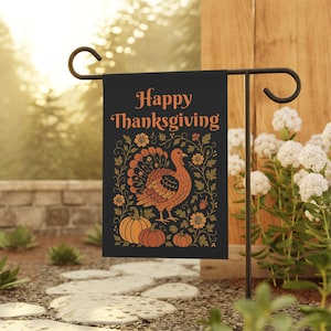 Puede incluir: Bandera de jardín negra con las palabras "Happy Thanksgiving" en letras naranjas. La bandera presenta una ilustración de pavo con calabazas y detalles florales. La bandera se muestra en un soporte de metal negro en un jardín.