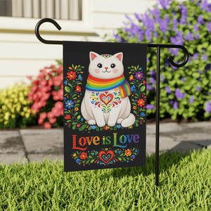 Może przedstawiać: Czarna flaga ogrodowa z białym kotem w tęczowym szaliku i wzorem serca. Flaga głosi "Love is Love" w kolorowych literach i jest otoczona kwiatowymi wzorami.