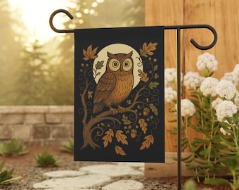 May include: A black garden flag featuring a detailed illustration of a brown owl perched on a branch, set against a full moon. The design includes autumn leaves in shades of brown and gold, creating a nature-themed aesthetic. The flag is displayed on a black metal stand.