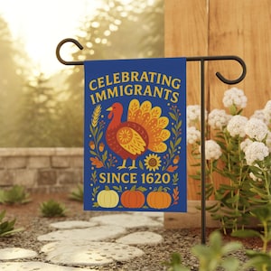 May include: A blue garden flag with the text "Celebrating Immigrants Since 1620" in yellow. The flag features a turkey illustration with a sunflower, pumpkins, and floral elements. The flag is displayed on a black metal stand.