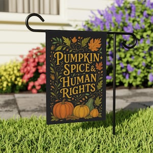 以下が含まれることがあります： 黒いガーデンフラッグ。金色の文字で「PUMPKIN SPICE & HUMAN RIGHTS」と書かれています。オレンジ、黄色、緑色のカボチャ、葉、つるのイラストが描かれています。芝生の庭にある黒い金属製のスタンドにフラッグが飾られています。