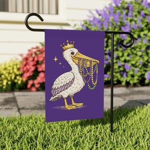 Könnte beinhalten: Eine lila Gartenflagge zeigt einen Cartoon-Pelikan mit einer goldenen Krone und bunten Perlen im Schnabel. Der Pelikan ist weiß mit gelben Füßen und einem lila Flügel. Zwei Sterne befinden sich neben dem Pelikan.