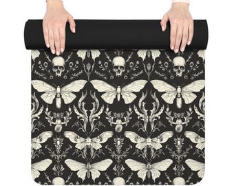 Op de afbeelding: Zwarte yogamat met een herhalend patroon van crèmekleurige motten, schedels en botanische elementen. De mat heeft een zwarte gerolde rand.