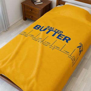May include: A yellow bedspread featuring the words "SALTED BUTTER" in blue. It includes a measuring guide with tablespoon and cup measurements. The grade is marked as AA.