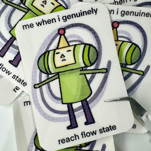 May include: A stack of white stickers featuring a green cartoon character with a yellow crown and a red ball on top. The text "me when I genuinely reach flow state" is printed on the stickers.