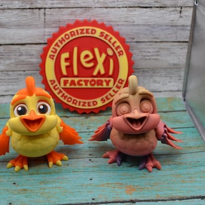 以下が含まれることがあります： 2羽の小さなカラフルな3Dプリントされた漫画の鳥の置物。左側の鳥はオレンジ色の羽と明るい黄色のくちばしを持つ黄色。右側の鳥はオレンジ色の羽とピンクのくちばしを持つピンク。両方の鳥は大きく丸い目を持っている。鳥たちは「Authorized Seller Flexi Factory Authorized Seller」と書かれた赤と黄色のステッカーのある木製の表面に座っている。