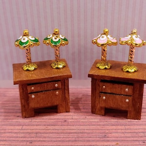 May include: Two miniature wooden nightstands with two drawers each. Each nightstand has a miniature lamp with a gold base and a white and green or white and pink shade.