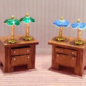 May include: Two wooden nightstands with two drawers each. Each nightstand has two matching lamps with floral-shaped shades. One set of lamps has green shades and the other set has blue shades.