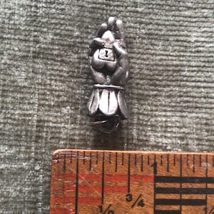 May include: A small, silver-toned charm in the shape of a hand holding a heart-shaped lock. The charm is approximately 1 inch in length. The charm has a detailed design and is set against a textured, green background.