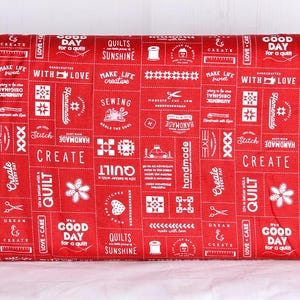 May include: Red fabric with a white patchwork design featuring sewing-related text and graphics. The fabric includes words like "handmade," "create," and "quilt," along with images of scissors, flowers, and sewing machines.