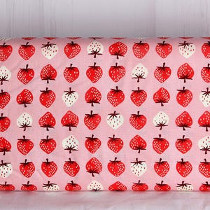 May include: Pink fabric with a repeating pattern of red and white strawberries. The strawberries have green stems and are evenly spaced across the fabric. This fabric is suitable for various sewing and crafting projects.