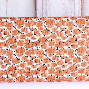 May include: White fabric with a repeating pattern of orange pumpkins with black stems and leaves. The pumpkins are outlined in black and have a dotted pattern.