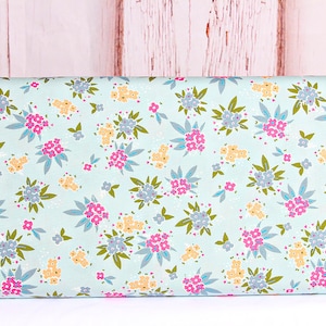 May include: A light blue fabric with a floral pattern. The pattern features small pink, yellow, and blue flowers with green leaves. The fabric has a subtle speckled texture.