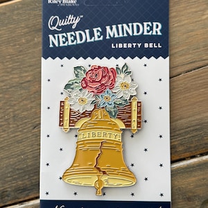 May include: A "Quilty Needle Minder" pin featuring the Liberty Bell with floral accents. The pin is gold with a crack down the center, and the text "LIBERTY" is visible. The card reads "Never lose another needle!"