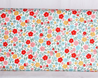 May include: A roll of floral fabric featuring a dense pattern of red, pink, yellow, and blue flowers with green leaves on a white background. The fabric is tightly rolled, showcasing the repeating floral design.