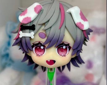 May include: A Nendoroid figure head with gray hair featuring pink highlights, two white and pink cow-print ears, and a black and white bone-shaped hair clip. The face has large pink eyes, a small open mouth, and a purple spot on the forehead.