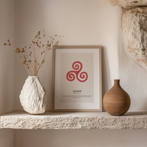 Könnte beinhalten: Ein gerahmter Druck mit einem roten Triskelion-Symbol und griechischem Text, der auf einem Steinsims ausgestellt ist. Eine weiße, strukturierte Vase mit Trockenblumen und eine braune Keramikvase stehen auf dem Regal. Der Hintergrund ist eine neutral getönte Wand.