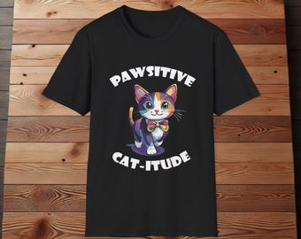Puede incluir: Camiseta negra con un gato de dibujos animados colorido que lleva una pajarita. El texto "Pawsitive Cat-itude" está impreso en la camiseta.