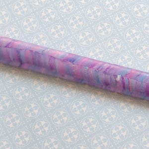 May include: A marbled pen with a purple, pink, and blue color scheme. The pen has a gold-colored tip and a white shaft. The pen is designed for diamond painting and other crafts.