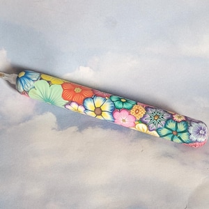 May include: A colorful flower-patterned tool for diamond painting, with a pointed tip and a white base.