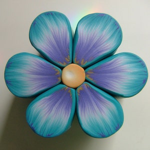 May include: A six-petal flower made of polymer clay. The petals are a gradient of teal and purple. The center of the flower is a light brown circle.