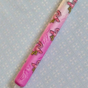 May include: A pink and white pen with a flamingo pattern. The pen has a gradient effect, transitioning from white to pink. The flamingo design is repeated along the pen's length.