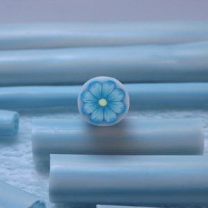 May include: A close-up of a blue and white polymer clay cane with a blue flower design. The cane is about 1/2 inch in diameter and is perfect for making jewelry or other crafts.