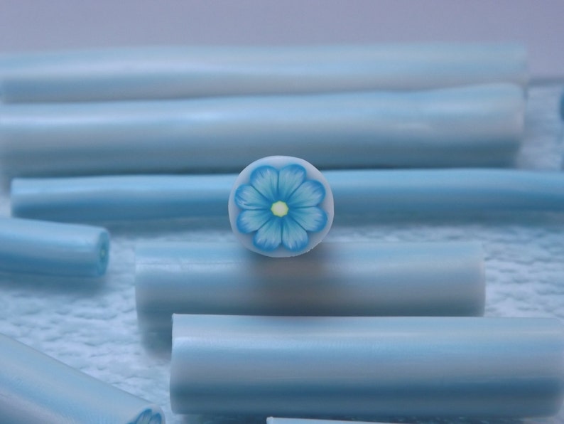 May include: A close-up of a blue and white polymer clay cane with a blue flower design. The cane is about 1/2 inch in diameter and is perfect for making jewelry or other crafts.