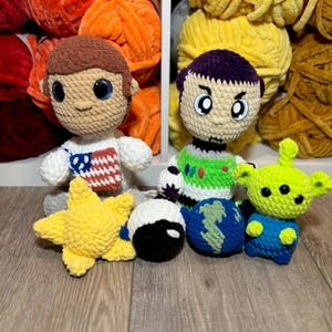 May include: A collection of handmade crochet dolls and accessories. The dolls include a character in a white spacesuit with an American flag design, and a character in a green and white outfit. Other items include a yellow star, a black and white ball, a blue globe, and a green alien.