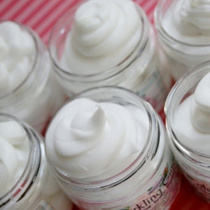 May include: Six glass jars filled with white body butter. The jars are labeled with different scents, including "Vanilla Body Butter" and "Black Kling"
