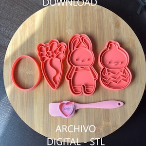 Puede incluir: Cortadores de galletas rosas con temática de Pascua en forma de huevo, zanahoria, conejito y pollito, junto con una espátula rosa. Las palabras "DIGITAL FILE - STL DOWNLOAD" y "ARCHIVO DIGITAL - STL" están impresas.